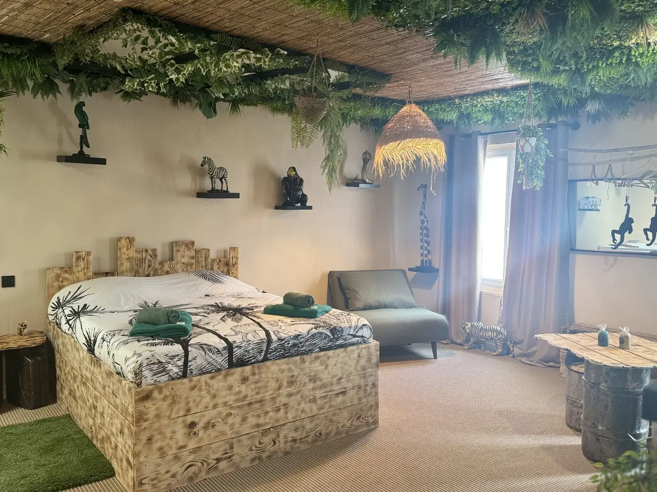 Suite La Jungle de Sissy avec décoration tropicale : lit en bois, plafond végétal, décorations d'animaux exotiques, et mobilier en bois naturel.